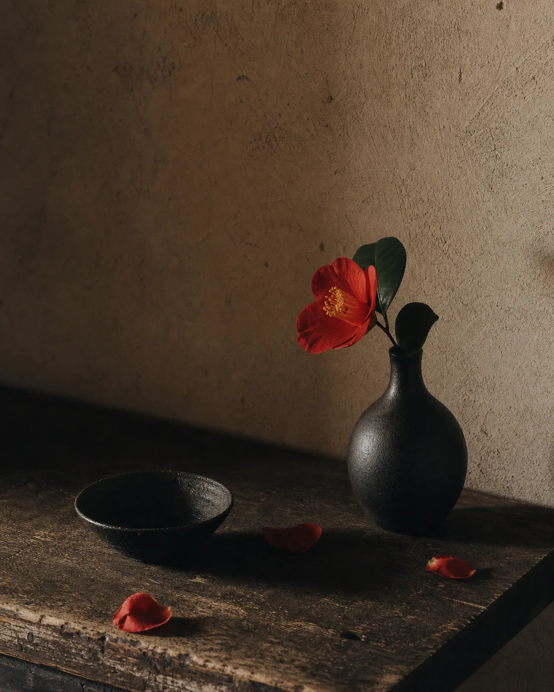 A dark ceramic still life with one red flower.